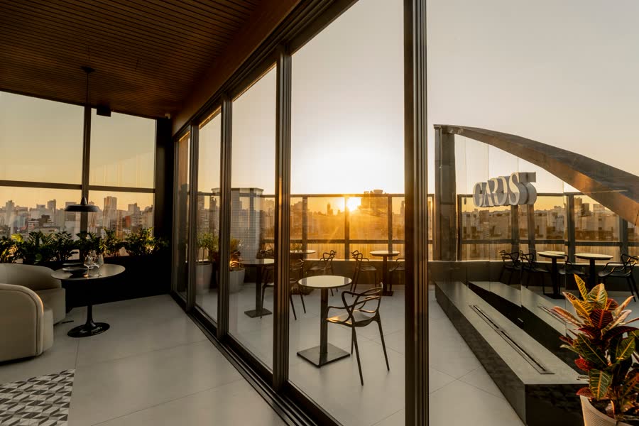 Terraço aberto com mesas e o sol se pondo entre os prédios